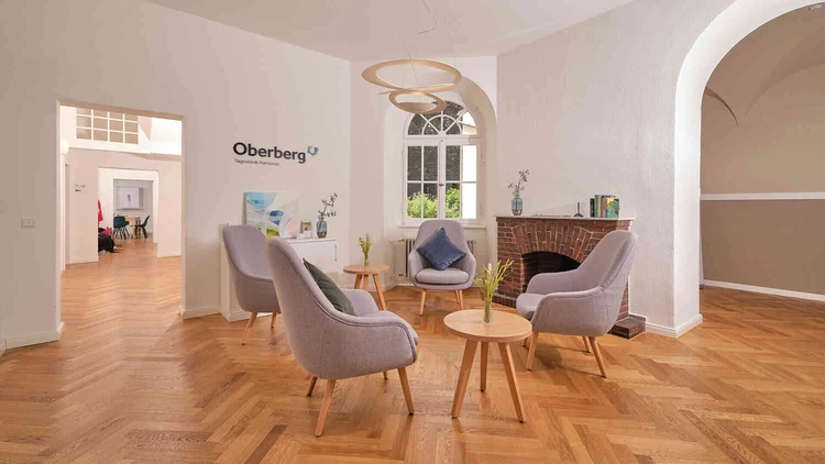 Heller Wartebereich der Oberberg Tagesklinik Hannover mit Sesseln, Kamin und Holzfu&szlig;boden
