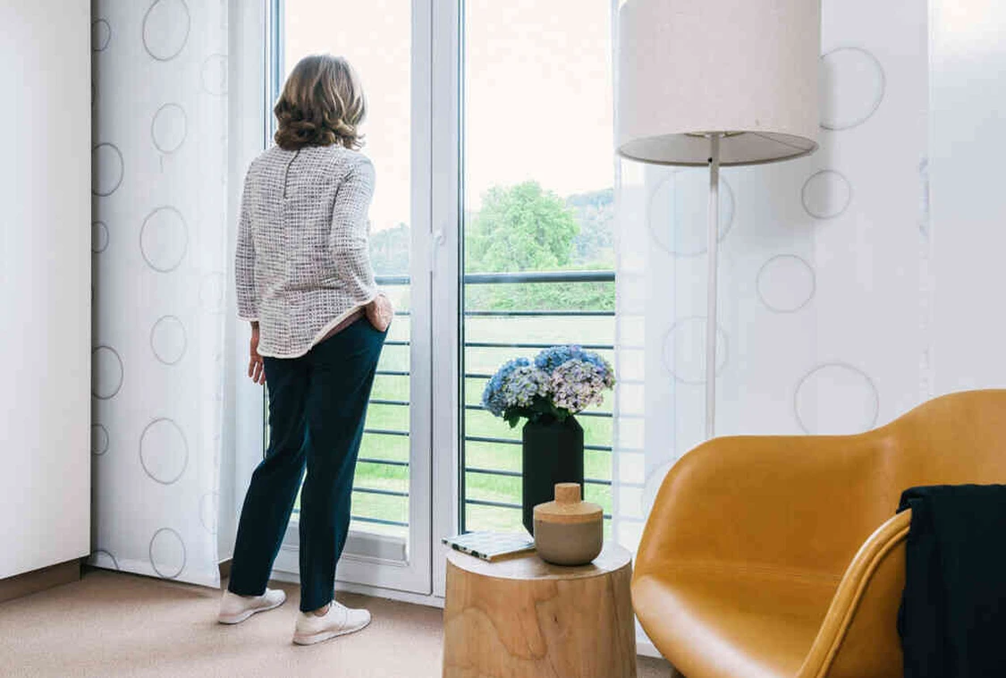 Frau steht am Fenster der Oberberg Fachklinik Weserbergland mit Blick ins Gr&uuml;ne