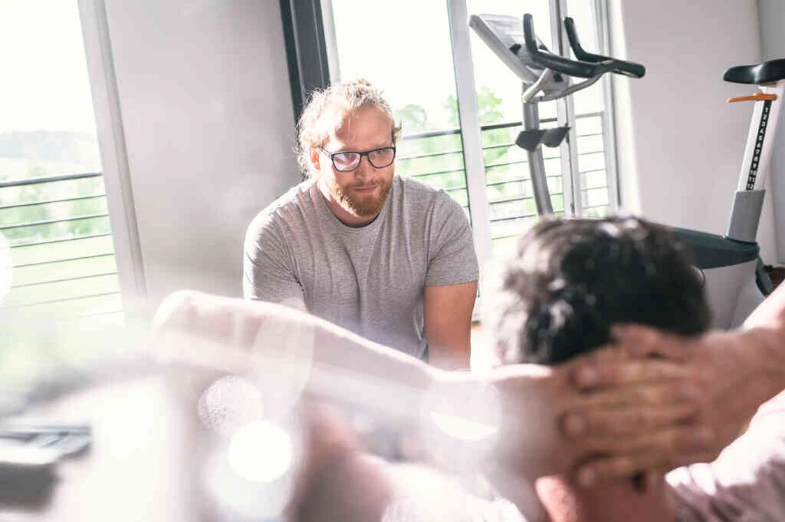 Mann mit Brille begleitet eine &Uuml;bung an einem Trainingsger&auml;t