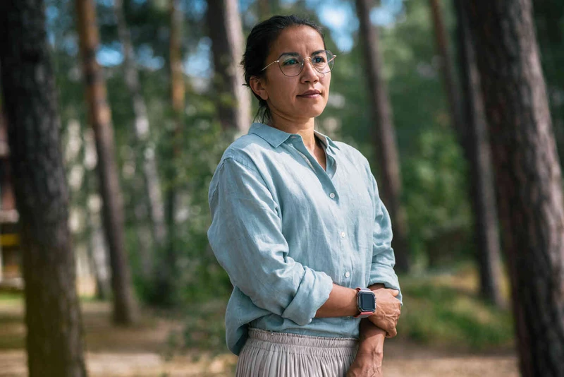 Frau mit Brille steht mit verschr&auml;nkten Armen in einem Waldst&uuml;ck