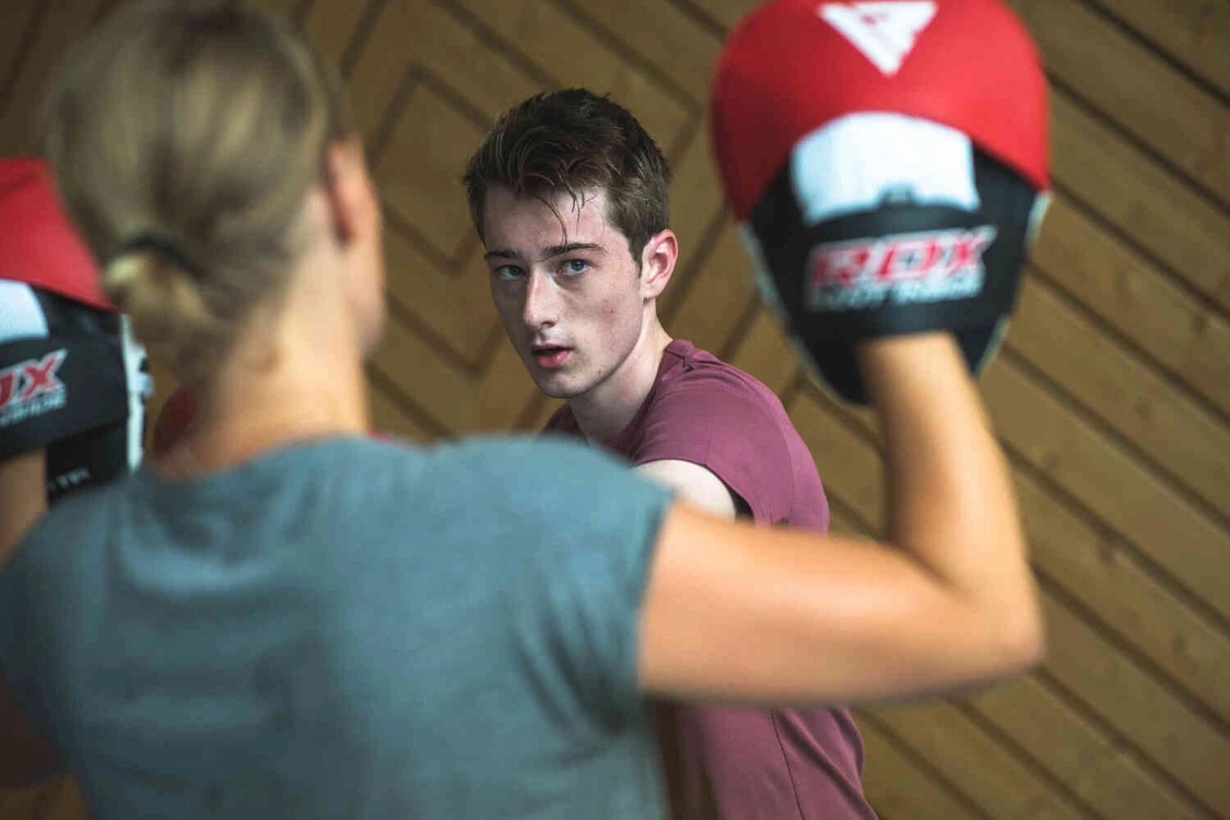 Junger Mann beim Boxtraining mit einer Person, die Pratzen h&auml;lt