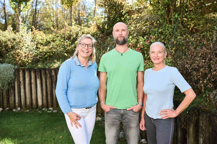 Drei Personen stehen gemeinsam im Garten