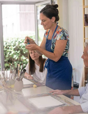 Person erkl&auml;rt in einer kleinen Gruppe etwas an einem Tisch im Rahmen der Kunsttherapie