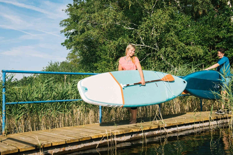 Zwei Personen tragen Stand-up-Paddle-Boards am See
