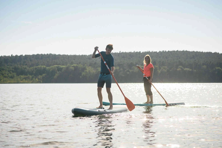 Zwei Personen stehen mit Stand-up-Paddle-Boards auf einem See