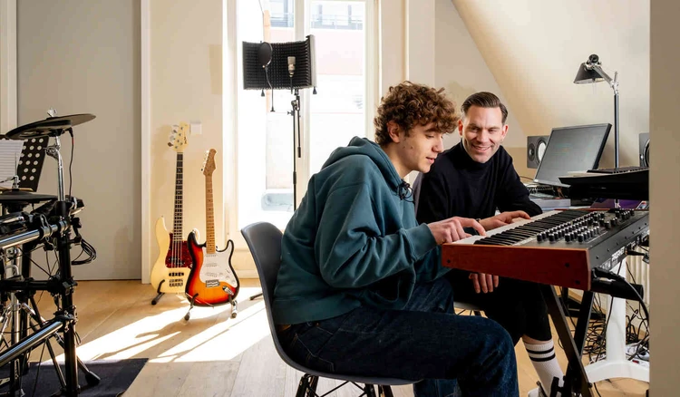 Junger Mann sitzt am Keyboard in einem Musikraum