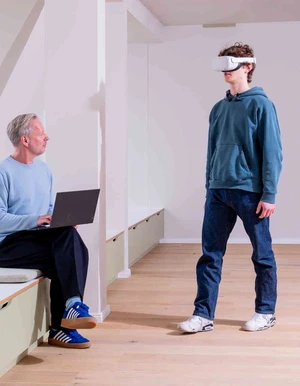 Mann mit Laptop sitzt vor Jungen mit VR-Brille