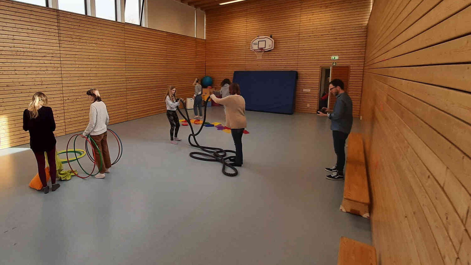 Personen stehen in einer Turnhalle mit Bewegungsmaterialien