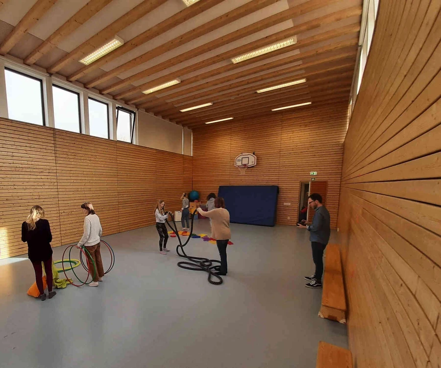 Personen stehen in einer Turnhalle mit Bewegungsmaterialien