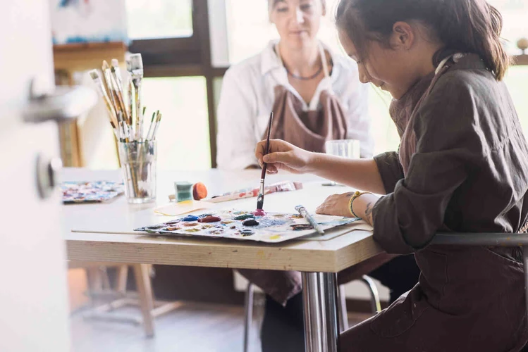 Zwei Personen arbeiten mit Malmaterialien an einem Tisch