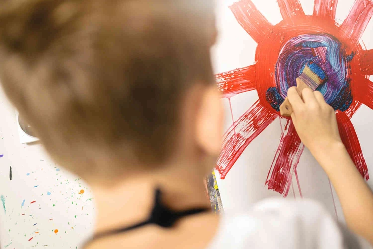 Junge Person malt mit roter Farbe auf Papier