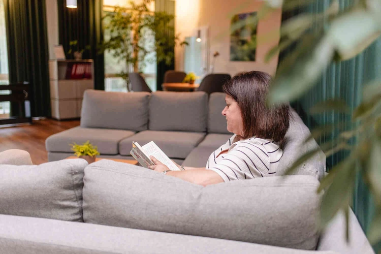 Person sitzt lesend auf einem Sofa in einem Aufenthaltsraum