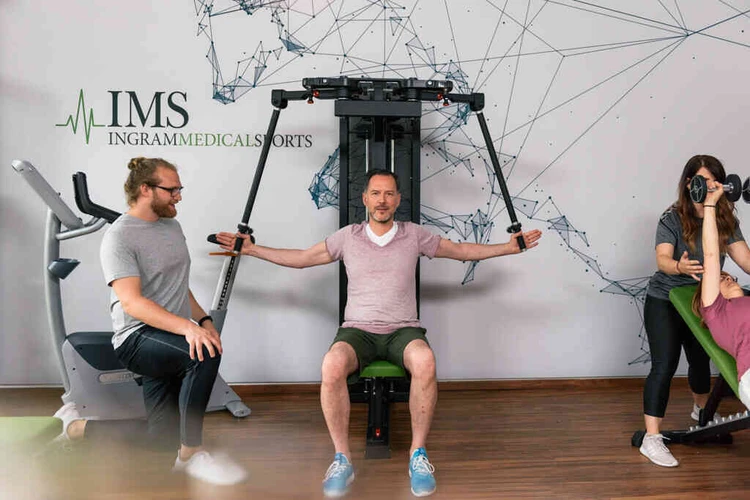 Mann begleitet eine Person bei einer &Uuml;bung im Fitnessraum