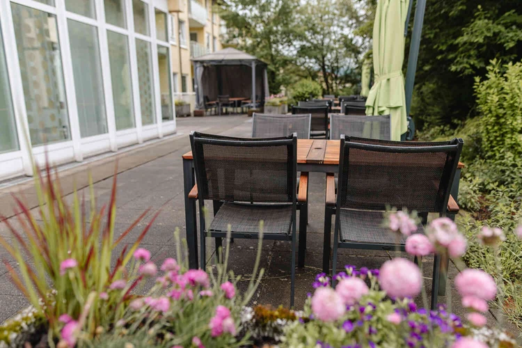 Terrasse mit Tischen und Sonnenschirmen in einer gr&uuml;nen Au&szlig;enanlage