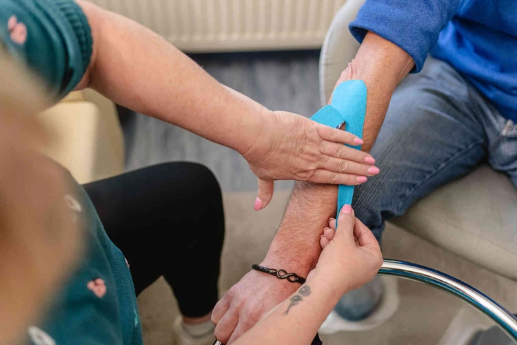Person bringt blaues Kinesio-Tape am Unterarm einer sitzenden Person an