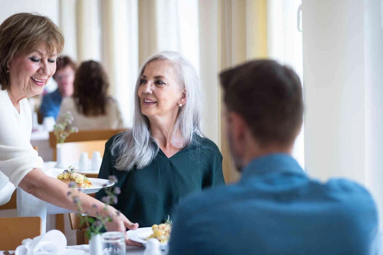 Personen sitzen an einem gedeckten Tisch in einem hellen Speiseraum
