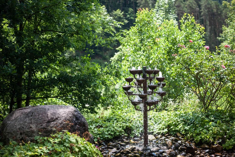 Mehrst&ouml;ckiger Gartenbrunnen zwischen Steinen und Pflanzen im Gr&uuml;nen