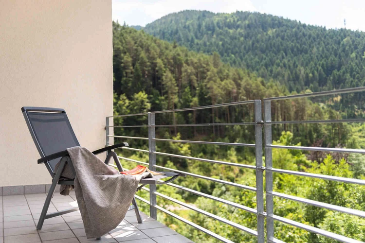 Balkon mit Stuhl und Blick auf bewaldete H&uuml;gel