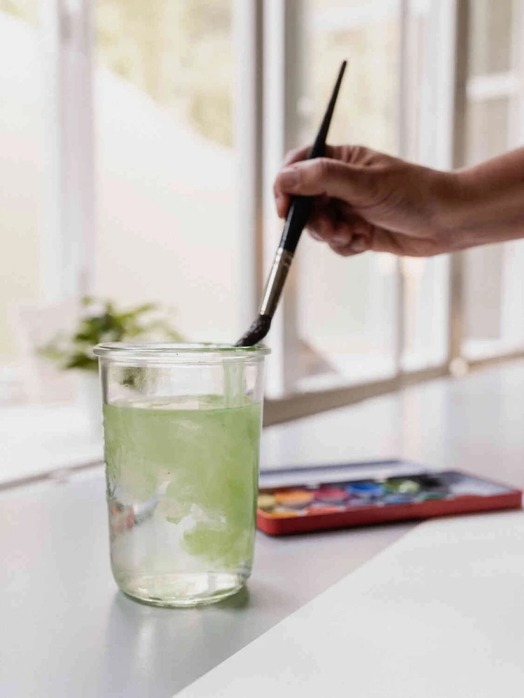 Hand r&uuml;hrt in einem Glas mit Wasser einen Pinsel aus