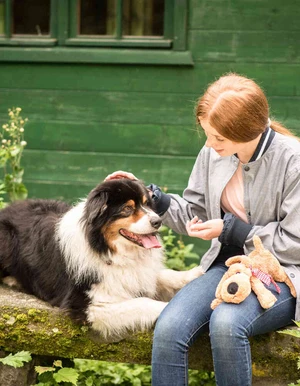 Junge Person sitzt mit einem Hund im Gr&uuml;nen