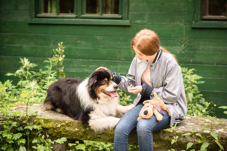Junge Person sitzt mit einem Hund im Gr&uuml;nen