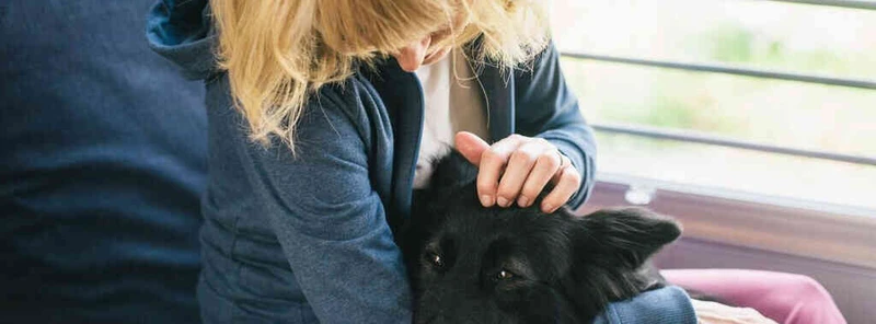 blonde Frau sitzt vor einem Fenster, schwarzen Hund auf ihrem Scho&szlig;