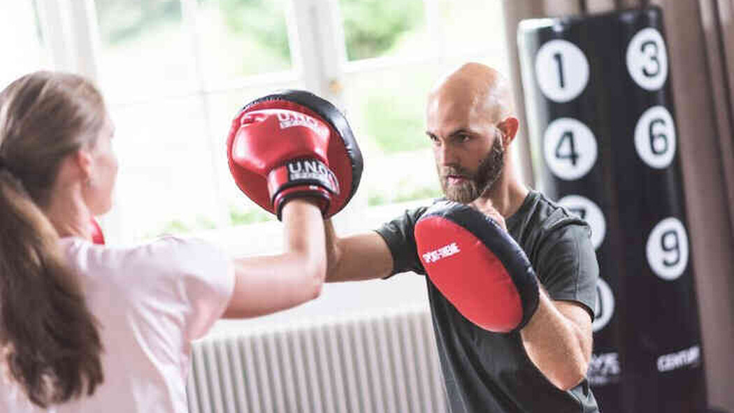 Trainer h&auml;lt einer Frau beim Boxtraining Pratzen hin