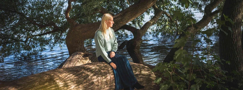 Blonde Frau sitzt auf einem gro&szlig;en Baumstamm am Ufer