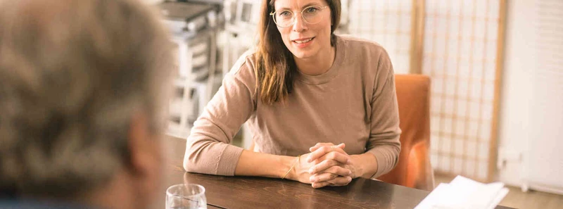 Frau sitzt in einem hellen Raum an einem Tisch im Gespr&auml;ch