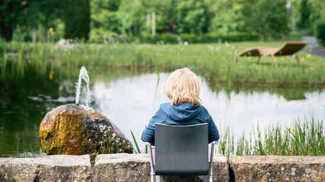 Person sitzt auf einem Stuhl am Teich mit Springbrunnen