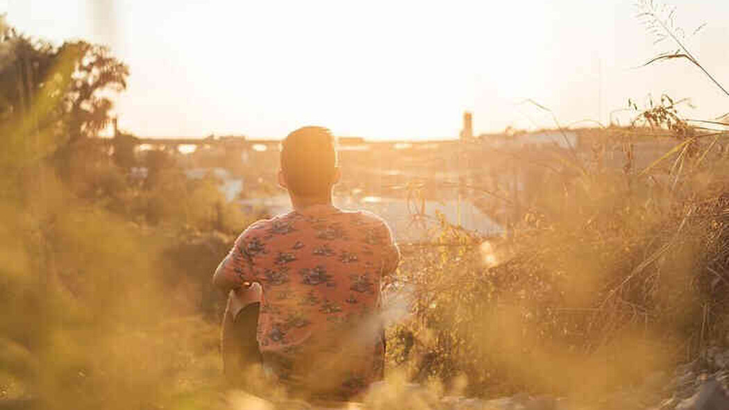 Mann sitzt bei Sonnenuntergang im Freien und blickt auf die Stadt