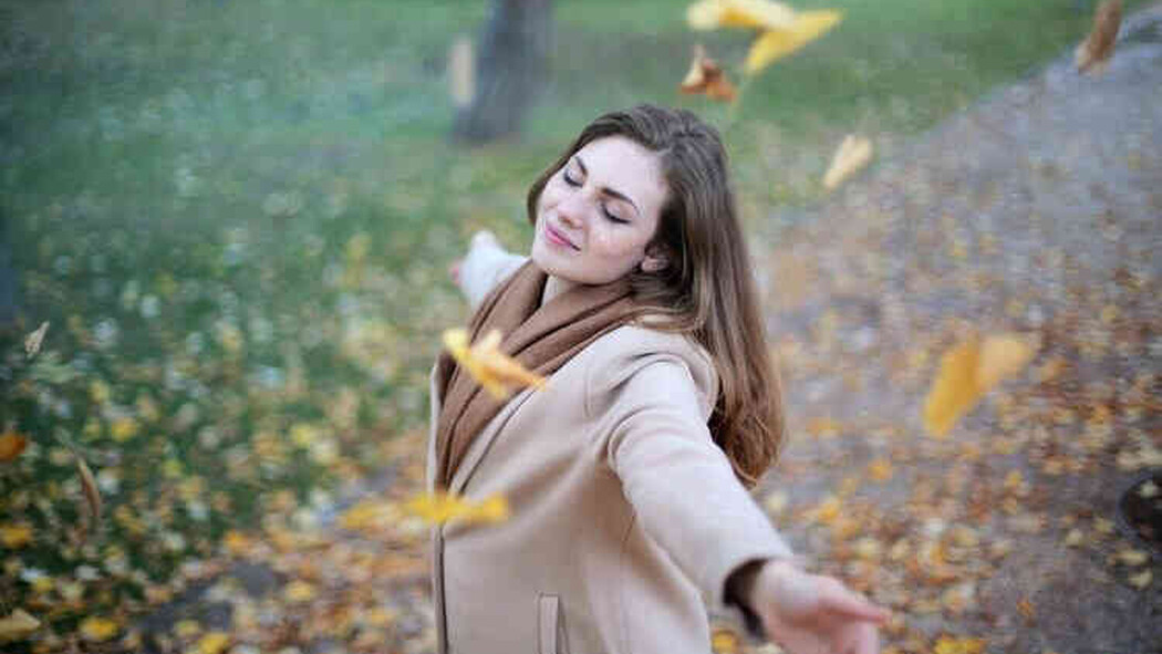 Frau steht mit geschlossenen Augen zwischen fallenden Bl&auml;ttern im Park
