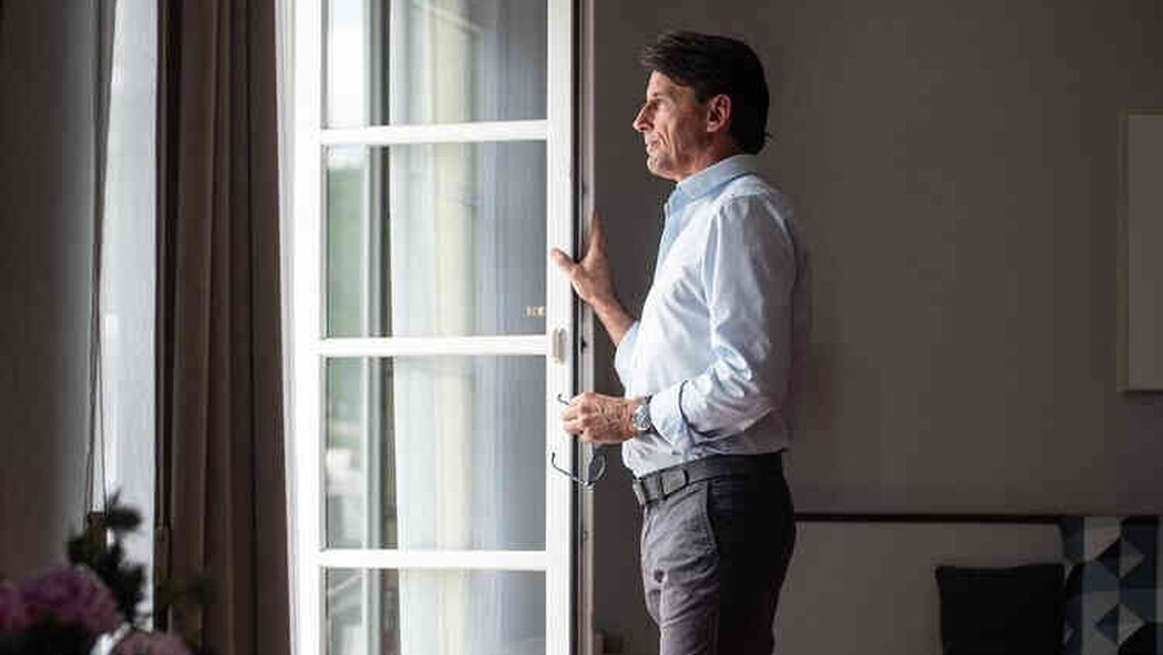 Mann steht am Fenster und blickt nach drau&szlig;en