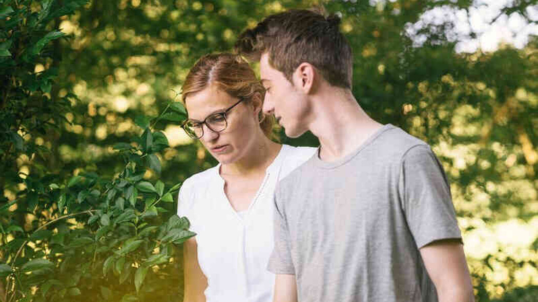 Frau mit Brille und junger Mann gehen nebeneinander im Gr&uuml;nen