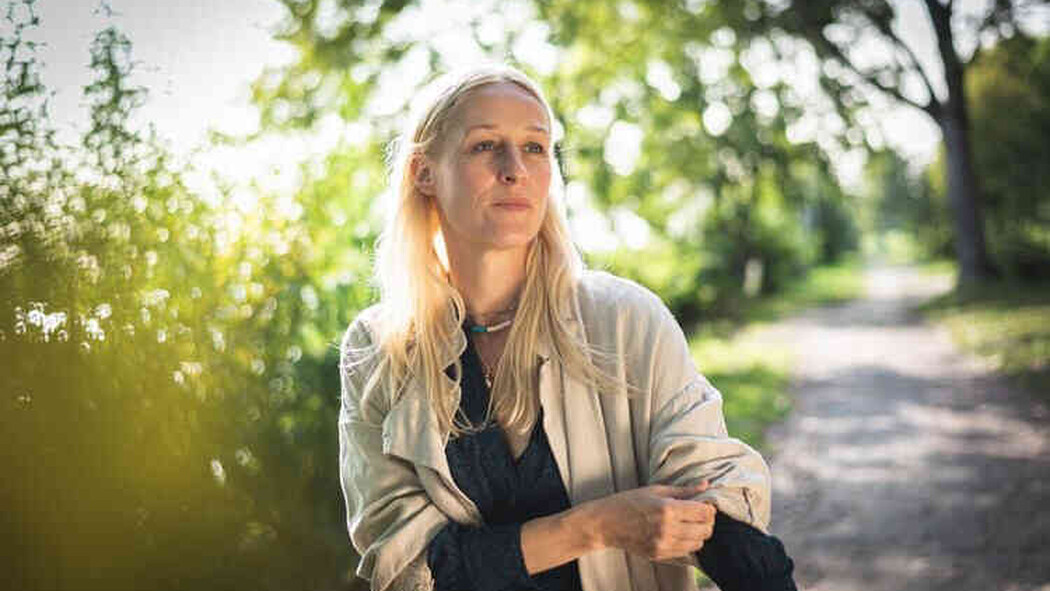Blonde Frau steht im Sonnenlicht auf einem Weg im Gr&uuml;nen